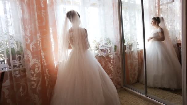 Красивая невеста в элегантном свадебном платье пешком к окну перед свадебной церемонией. вид сзади — стоковое видео