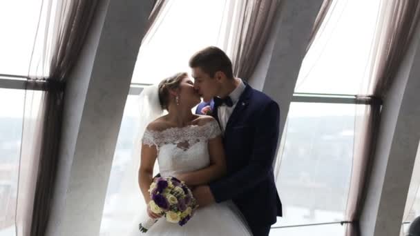 Sposo e sposa con mazzo di fiori che si baciano davanti alla finestra al coperto. Colpo al rallentatore — Video Stock