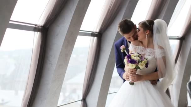 Groom and bride with flower bouquet kissing in front of the window indoor. Beautiful wedding dress. Just married Slow motion shot — Stock Video