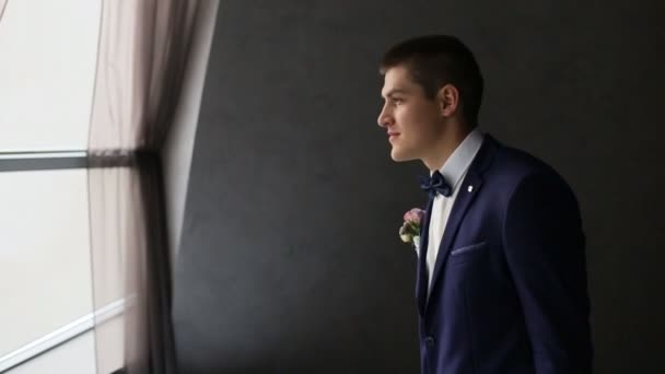 Groom marchant vers la fenêtre en beau costume bleu foncé. Homme regardant par la fenêtre — Video