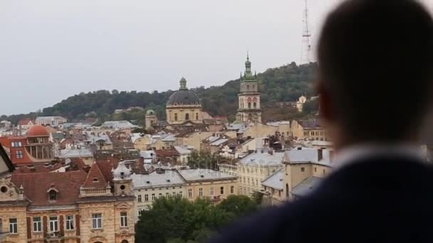 Los novios desenfocados atrás. Novio mirando el paisaje de la ciudad. Lviv. Ucrania. Vista panorámica de la ciudad desde arriba. Hermosos edificios antiguos de la ciudad. Antigüedad — Vídeo de stock