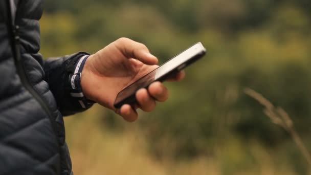 Hombre usando smartphone en el parque. De cerca la mano con el teléfono inteligente negro en el parque, al aire libre — Vídeos de Stock