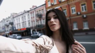 Gülümseyen kadın kentsel sokakta kendi fotoğraf çekme. Güzel beyaz esmer kız ile beyaz ceketli selfie yapar. Bir turist.