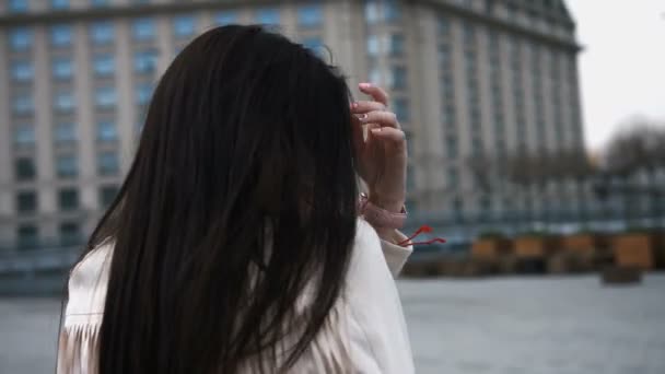 Joven hermosa mujer riendo caminando y corriendo, alegre y alegre sonriendo en un fondo de la ciudad. Chica vestida con chaqueta blanca — Vídeo de stock