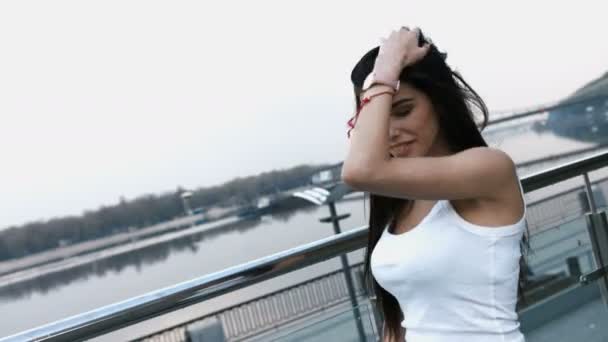 Hermosa encantadora joven morena en camisa blanca posando de pie en el puente de la ciudad moderna — Vídeos de Stock