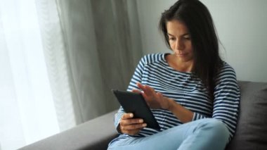 Güzel genç kadın sandalyede oturan ve evde tablet kullanma.