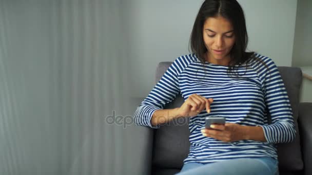 Jovem bela senhora sentada na cadeira e usando telefone celular em casa . — Vídeo de Stock