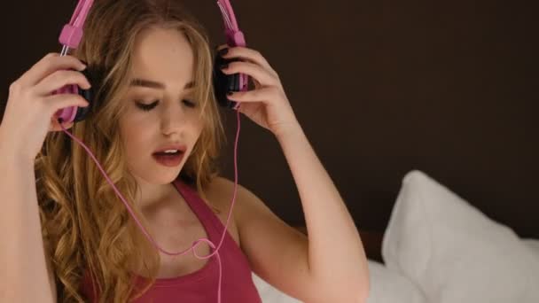 Lächelnde junge Frau hört Musik in ihrem modernen, sauberen Schlafzimmer. — Stockvideo