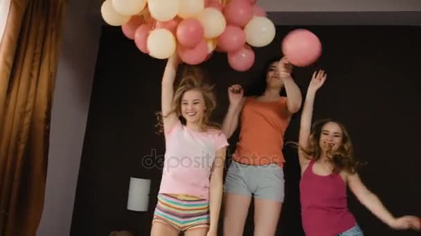 Legrační mladí přátelé krásné skákání na posteli s barevné balónky v rukou.