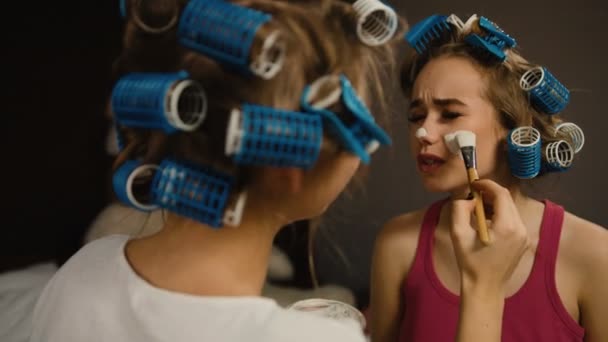 Dos hermosos jóvenes amigos con rizadores de pelo haciendo máscaras en la cara . — Vídeo de stock