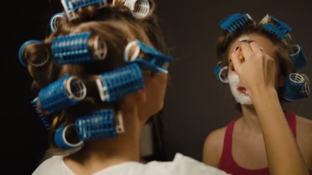 Two beautiful young friends with hair-curlers making masques on face. — Stock Video