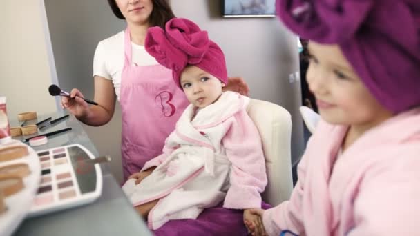 Çok küçük kızlar el ele tutuşarak. Salonda güzel küçük kızlar için yapmak yapıyor sanatçı makyaj — Stok video