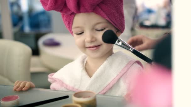 Hermosa niñita en el salón. Maquillaje artista haciendo maquillaje con gran cepillo para niña bonita — Vídeo de stock