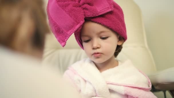 Красивая маленькая девочка в розовом халате и полотенце на голове в профессиональном салоне — стоковое видео