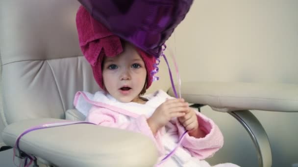 Hermosa niña sosteniendo globos en el salón. Vista de cerca bonita niña en bata rosa en salón profesional — Vídeo de stock