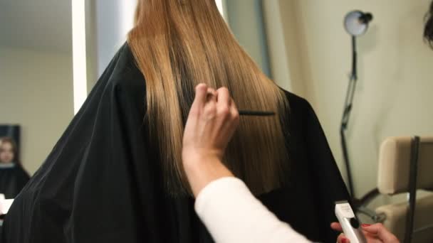 Профессиональный парикмахер стрижет длинных блондинок с триммером в салоне красоты . — стоковое видео