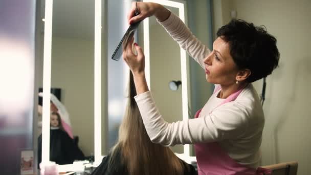 Profesjonalny salon fryzjerski cięcia dziewczyn długie blond włosy nożyczkami w gabinecie kosmetycznym. Stylista robi fryzurę — Wideo stockowe