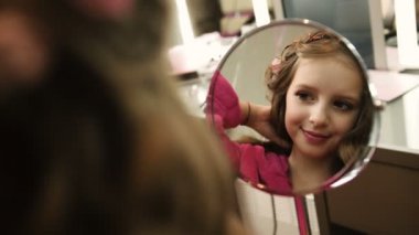 Sevimli küçük kız Güzellik Salonu aynaya bakarak kıvırcık saçlı. Aynaya görüntülemek