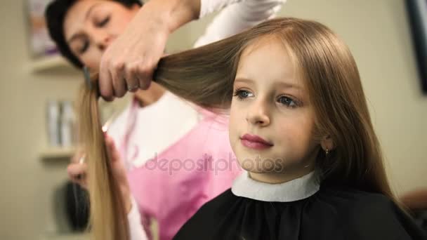 Крупним планом професійний перукар, що ріже довге світле волосся для дівчаток з ножицями в салоні краси. Стиліст робить зачіску — стокове відео