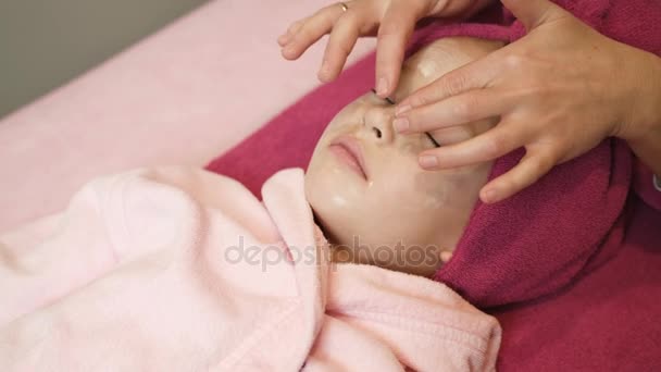 专业的美容师应用在美容院的美丽小女孩脸上的面具。温泉疗法。关闭了视图 — 图库视频影像