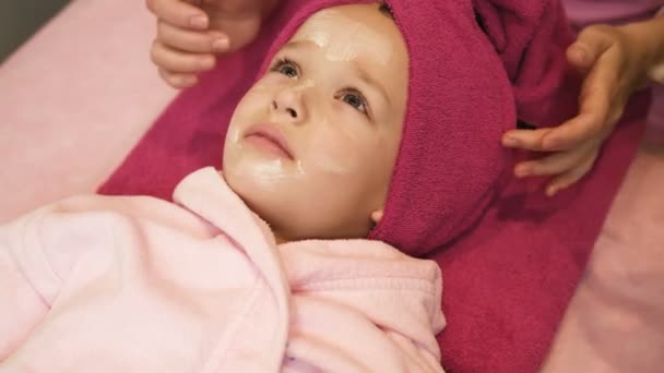 Professionell kosmetolog applicera masken på lilla flickor ansikte på skönhetssalongen. Spa behandling. Nära håll view — Stockvideo