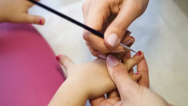 Artista de uñas haciendo manicura para niña en el salón profesional. Vista de cerca del maestro de la manicura aplicando gel esmalte y haciendo puntos. Manos cerca de la vista — Vídeo de stock