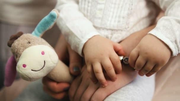 Vista de cerca de la niña bonita sentada en las rodillas de las madres y jugando con su pulsera en el salón de belleza. Vista de cerca . — Vídeo de stock