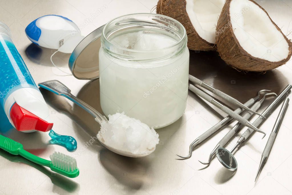 Selection of dentists tools on a stainless steel background with coconut oil, toothpaste, toothbrush and floss. Heaped dessert with cocunut oil by jar.