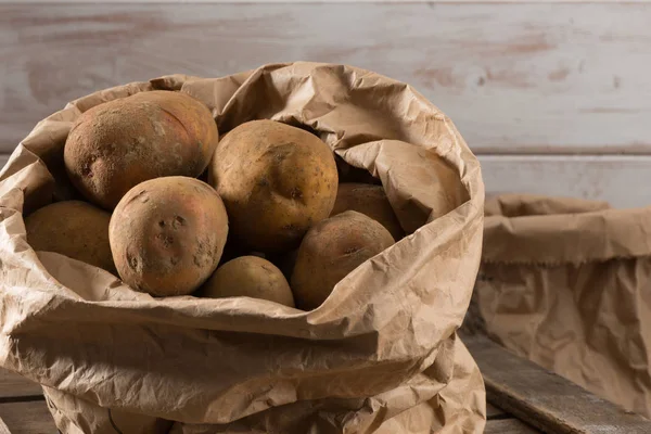 Organically grown potatoes in a paper bagon top of a wooden crate with white wooden board background