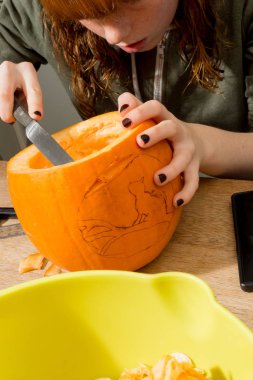 Genç bir kız bıçakla balkabağı oyuyor.