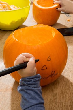 Toddler'ın eliyle balkabağına bir yüz çiziyor.