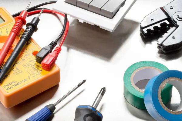 Selection of electrical contractors tools including wire cutters, multimeter, screwdrivers, electrical tape, clips and a light switch.