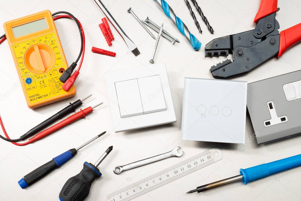 Various electrician tools and components including a multimeter, screwdrivers, wirecutters, drill bits, switches and sockets.