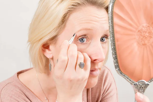Woman Holding and Facing a Mirror While Plucking Eyebrows — Stock Photo, Image