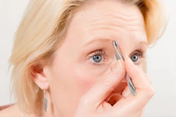 Close-up de mulher loira arrancando suas sobrancelhas — Fotografia de Stock