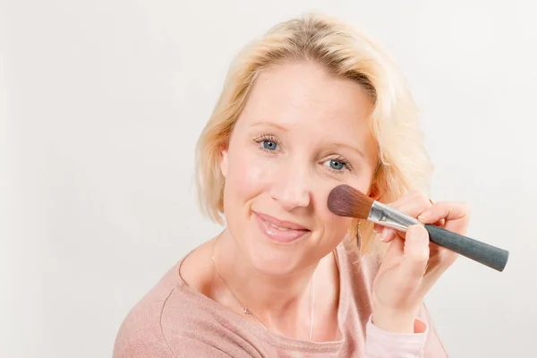 Senhora loira olhando diretamente e aplicando maquiagem na bochecha — Fotografia de Stock