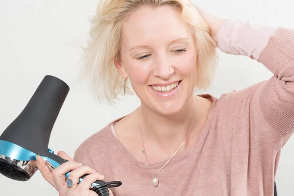 Bionda donna sorridente mentre asciuga i capelli utilizzando asciugatrice — Foto Stock
