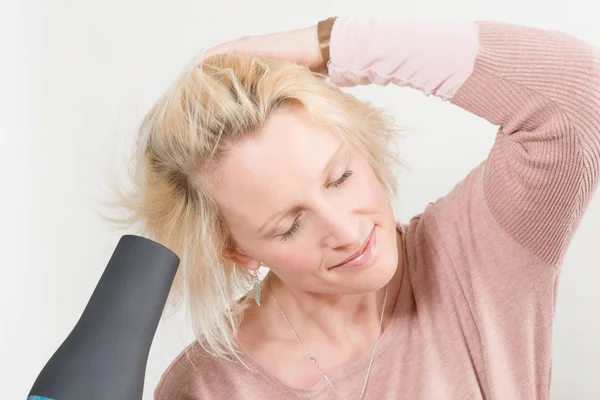 Mujer con los ojos cerrados mientras se seca el cabello con secador de pelo — Foto de Stock
