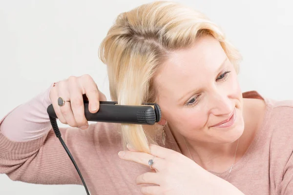 Rubia dama alisándose el pelo con una plancha — Foto de Stock