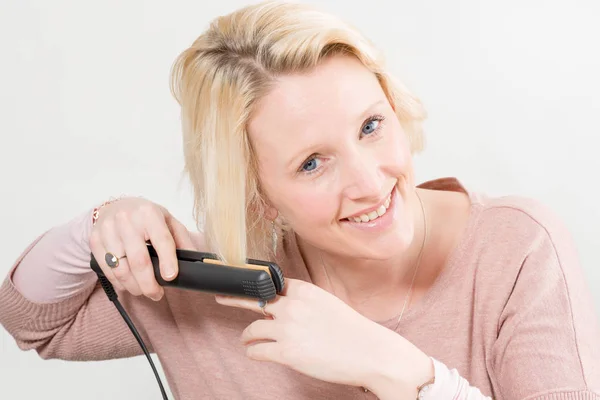 Sonriente dama peinándose el pelo con hierro — Foto de Stock