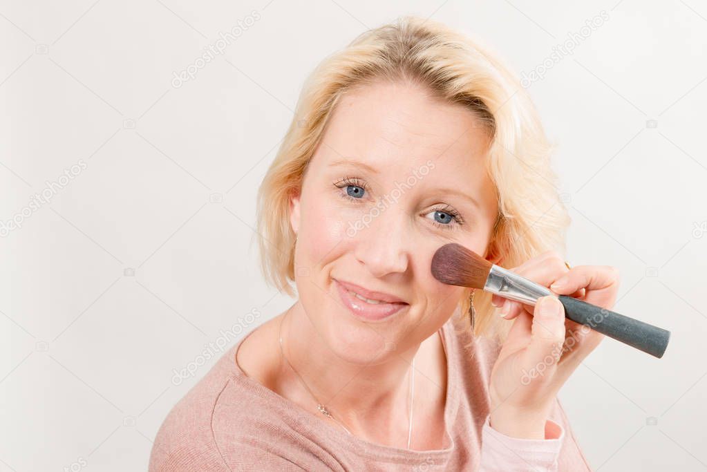 Blonde Lady Gazing Directly and Applying Make-Up on Cheek