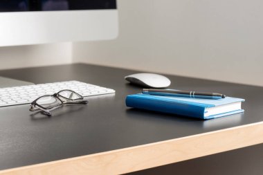 Gri Ofis Masası bilgisayar, gözlük, bir kalem ve defter 