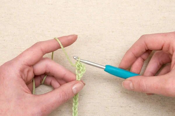 Mãos costurando uma corrente de fio verde usando gancho de tricô — Fotografia de Stock