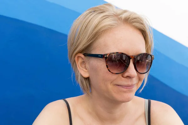 Donna sorridente che indossa occhiali da sole su sfondo onde blu — Foto Stock