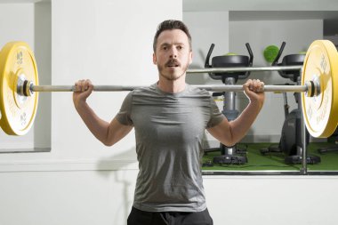 Omuzlarında ağır bir halter ile atletik adam