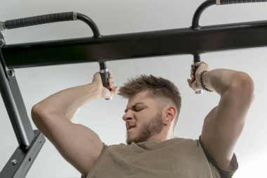 Genç adam Winces ve pazı Pull-up yaparken bakar