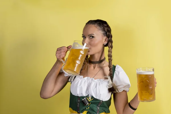 在裙喝啤酒从杯子在黄色背景的女孩 — 图库照片