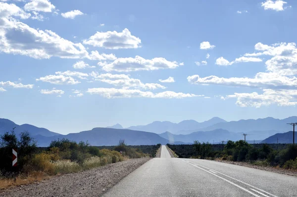 Auto-estrada sob céu azul ensolarado com gama de montanhas no horizonte — Fotografia de Stock