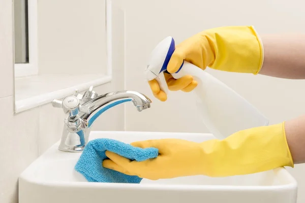 Руки в перчатках, брызгающие жидкое мыло на тряпку на раковину в ванной — стоковое фото