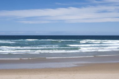 Plaj ve okyanus dalgaları bulutlu mavi gökyüzü altında